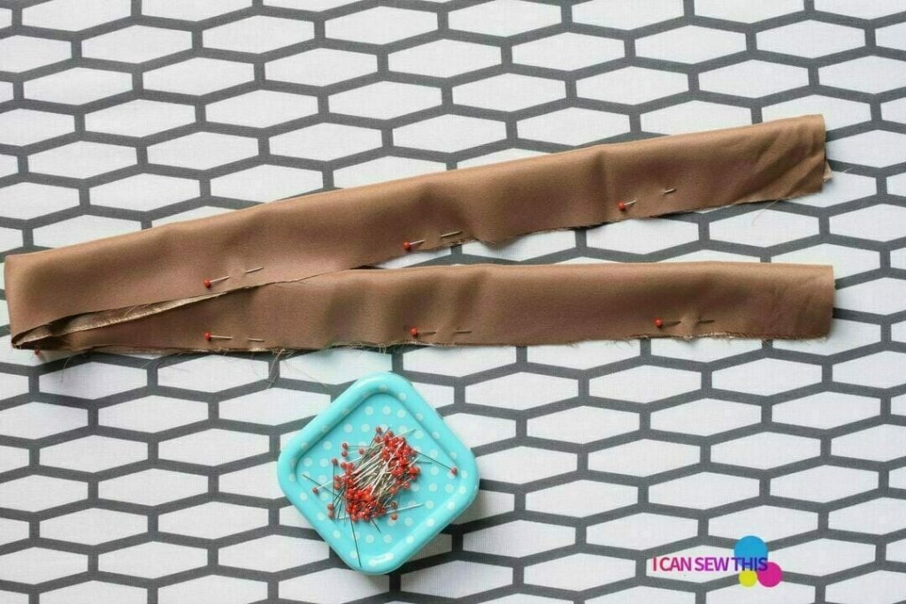 Folded satin fabric strip pinned lengthwise with sewing pins on a mat